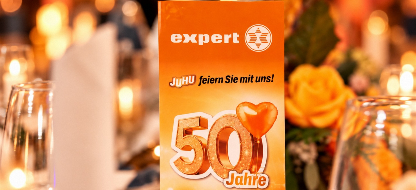 Orangefarbener Jubiläumsaufsteller von expert zum 50-jährigen Bestehen in festlicher Tischdekoration
