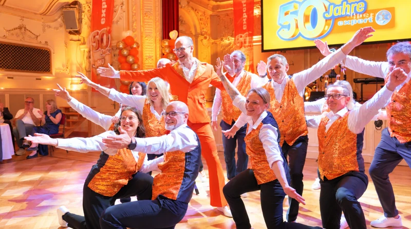 expert-Tanzteam in orange-goldenen Westen posiert mit ausgestreckten Armen beim Finale