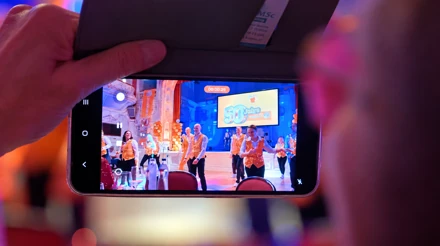 Smartphone zeigt die Aufnahme des expert-Tanzteams vor der Jubiläumsleinwand