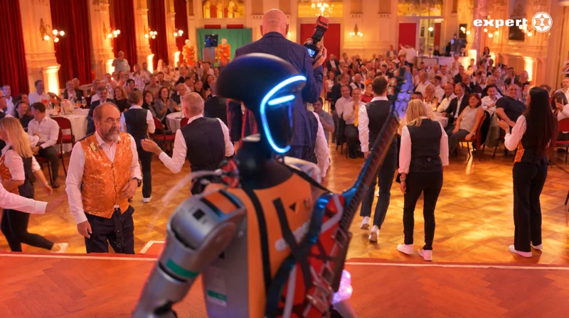 Blick hinter dem Unitree G1 auf das stehende Publikum und das Tanzteam im Festsaal