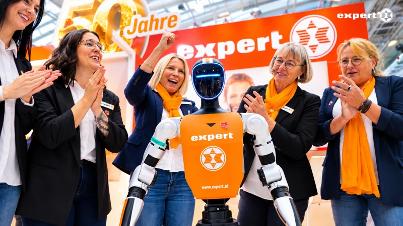 expert-Team mit orangefarbenen Schals applaudiert rund um den Unitree G1 am Messestand