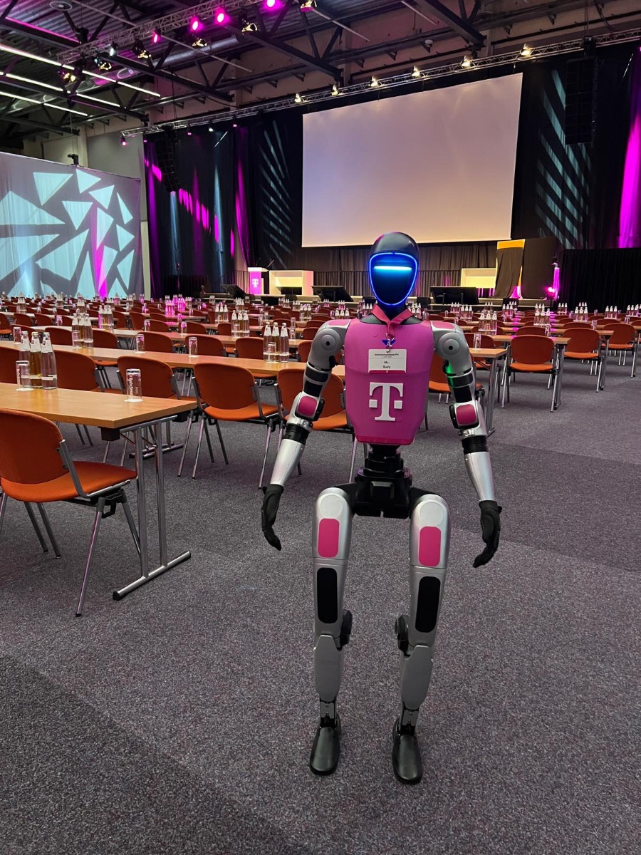 Mr. Buddy vor dem Saal der Telekom Betriebsversammlung mit Sitzreihen und Bühne