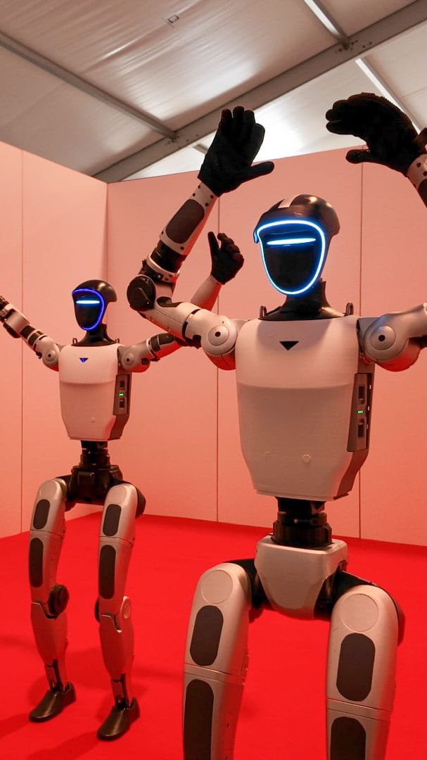 Zwei Unitree G1 Roboter vor rotem Bühnenhintergrund mit erhobenen Armen