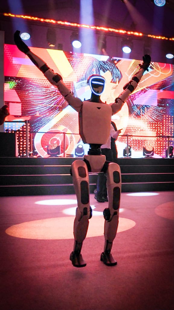 Unitree G1 Roboter mit erhobenen Armen vor farbiger Bühnenkulisse