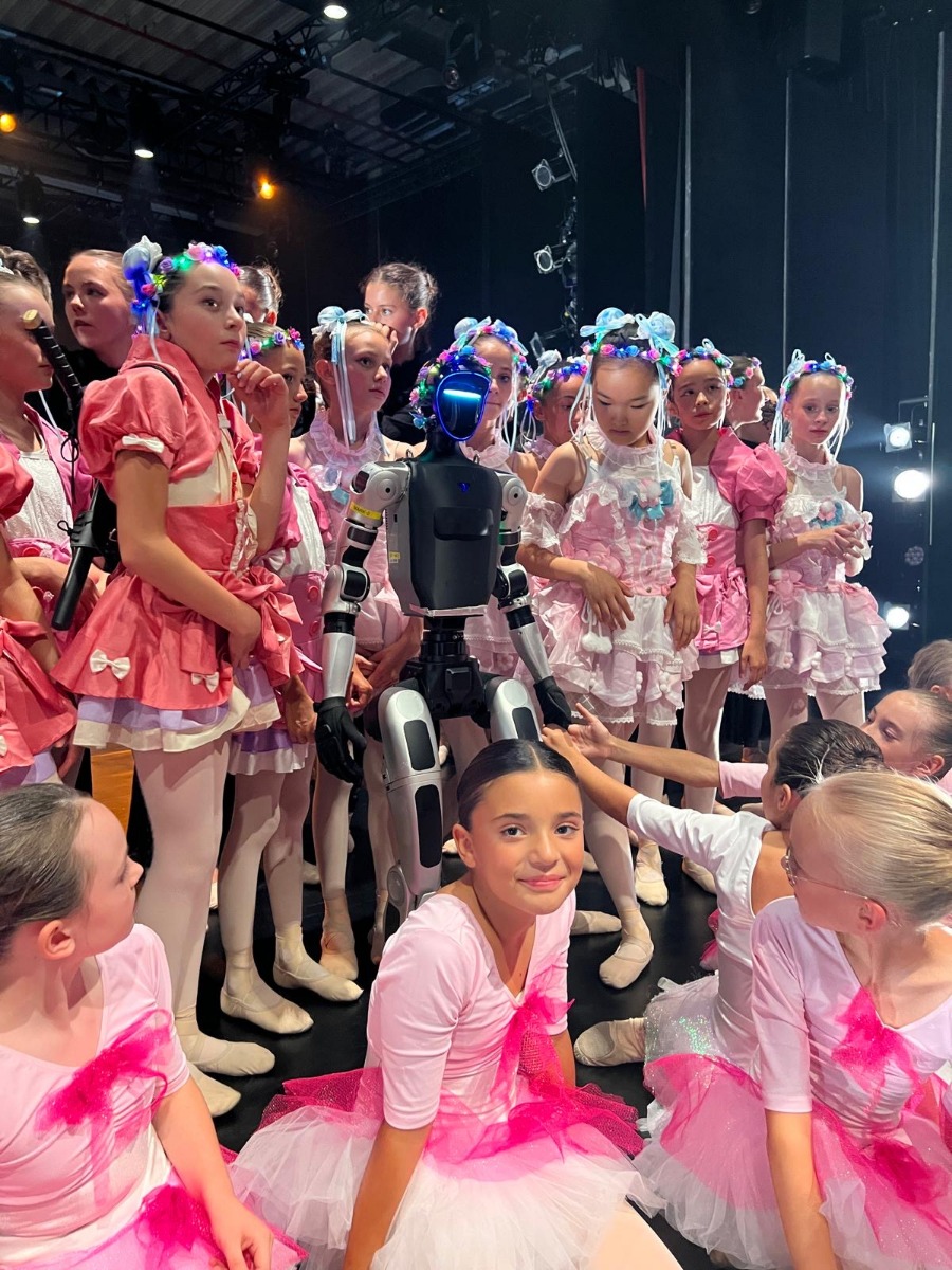 Unitree G1 inmitten junger Tänzerinnen in pink-weißen Kostümen im Staatstheater Augsburg