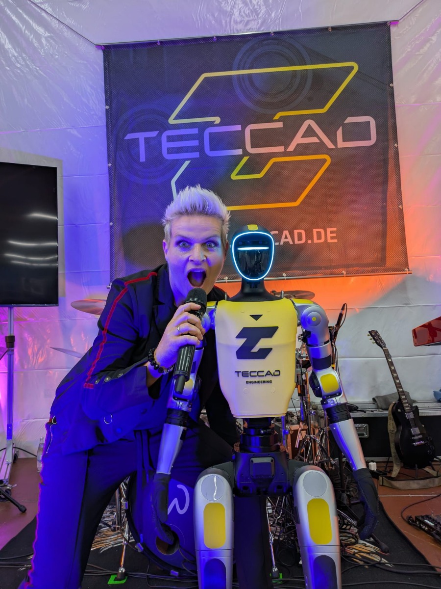 Sängerin mit Mikrofon neben humanoidem Roboter Alfons beim Bühnenfinale des TECCAD Jubiläums